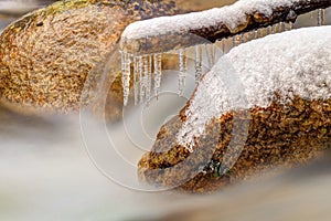 Smoky cold water of mountain stream in winter time. Long crystal icicles are hanging above milky water level.