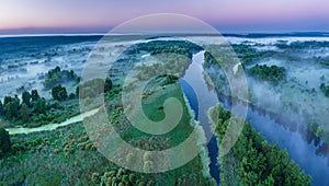 Smoky morning mist over the river. Beautiful panoramic view of river and green banks of the river in the early summer morning