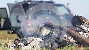 Smoldering campfire with and expeditionary suv on the background