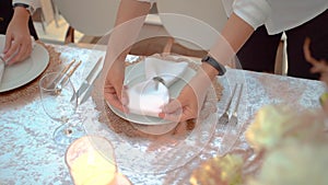 Smooth female hands with smart watch serve napkin in the form of bow, tightened by ring. Girl waitress neatly