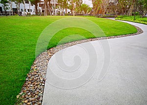 Smooth green grass lawn, trees with supporting and shrub in a good maintenance landscape and garden, gray curve pattern walkway