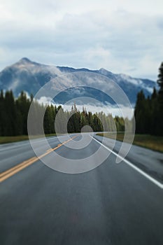 Smooth highway passing through a scenic forest; picturesque mountains in fog in the background