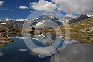 A smooth Riffelsee lake surface and mountains and clouds reflected in it, on a mountain Gornergrat, Switzerland