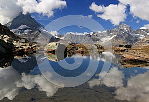 A smooth Riffelsee lake surface and mountains and clouds reflected in it, on a mountain Gornergrat, Switzerland