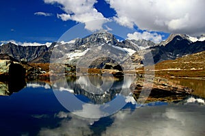 A smooth Riffelsee lake surface and mountains and clouds reflected in it, on a mountain Gornergrat in Switzerland