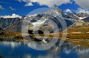 A smooth Riffelsee lake surface and mountains and clouds reflected in it, on a mountain Gornergrat, Switzerland