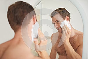 For a smooth shave.... A handsome young man applying shaving cream to his face in front of a mirror.