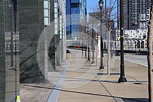 A smooth sidewalk lined with bare winter trees and tall black light posts and an empty street with office buildings