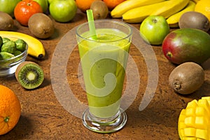 Smoothie banana kiwi mango orange and apple in glass on a brown table. Selected focus.