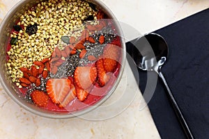 Smoothie bowl with blend fruits, strawberry, goji, chia seeds, and green buckwheat granola, and metal black spoon, on the table