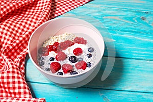 Smoothie bowl with chia seeds, muesli, jam and berries on blue wood background.