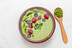 Smoothie bowl made of matcha green tea with fresh berries, nuts, seeds with a spoon for healthy vegan diet breakfast