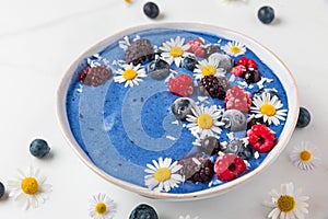 Smoothie bowl or nice cream made of blue spirulina, frozen berries, banana and coconut with chamomile flowers