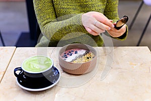 Smoothie bowl of raw food and matcha latte Cup of green tea on the table and a woman ready to eat