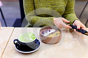 Smoothie bowl of raw food and matcha latte Cup of green tea on the table and a woman ready to eat. vertical photo