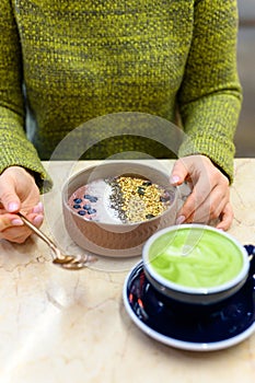 Smoothie bowl of raw food and matcha latte Cup of green tea on the table and a woman ready to eat. vertical photo