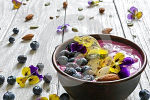 Smoothie bowl topped with fresh berries, banana, chia seeds, nuts and flowers for healthy vegetarian diet breakfast.