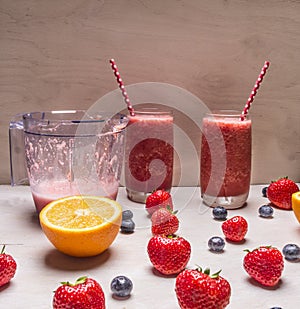 Smoothie of strawberries berries in glass jars with beautiful tubes on a white wooden table, around the expanded fresh strawbe