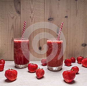 Smoothie of strawberries and berries in glass jars with beautiful tubes on a white wooden table, around expanded fresh strawbe