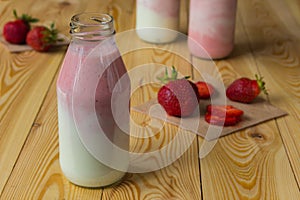 Smoothie with strawberry in bottles on wooden table