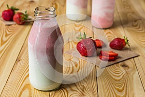 Smoothie with strawberry in bottles on wooden table