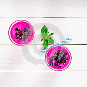 Smoothies of black currant in glass glasses with straws on a white wooden table. Top view.