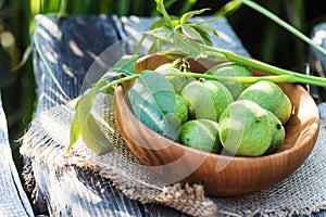 Smoothy unripe green walnuts and tincture of nuts in a transparent jar with a cork lid on an old vintage table. Leaves on branch