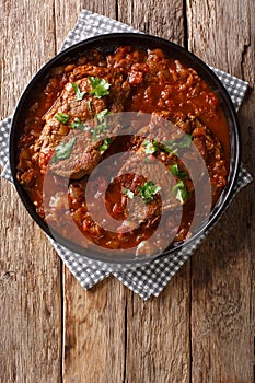 Smothered food Swiss steak in a spicy tomato sauce with vegetables close-up. Vertical top view