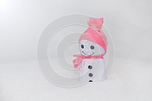 smowman standing on snow. handmade toy with pink fabric hat and white snowflakes- standing close up