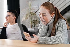 SMS. Closeup portrait funny shocked anxious scared young girl looking at phone seeing bad news photos message with