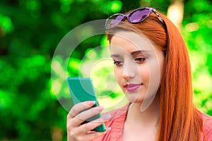 Sms. Smiling red head girl young woman texting video chatting talking looking at mobile phone profile view. In the park, outdoors