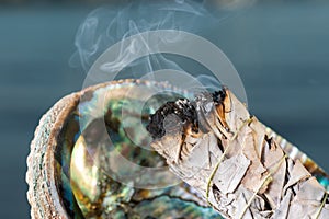 Smudging Ritual using burning thick leafy bundle of White Sage in bright polished Rainbow Abalone Shell on the beach at sunrise