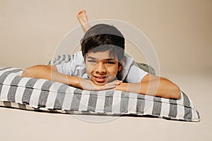 Smug indian boy lying on a striped mattress over beige background