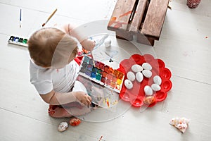 Smutty kid paints eggs on light background, photo