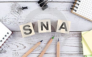 SNA text on wooden block with office tools on the wooden background