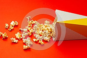 Snack concept, Sweet popcorn spilled out from paper cup on red background