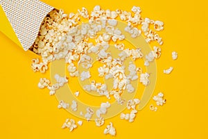 Snack concept, Sweet popcorn spilled out from paper cup on yellow background
