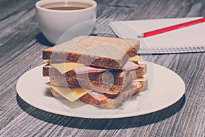 Snack education fast junk food concept. Business lunch. Tasty ham sandwich with cup of tea, notebook and a pencil. Vintage effect,