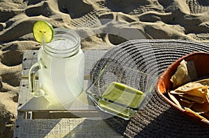 Snack of lemonade with lime slice, green salsa and tortilla chips at the beach