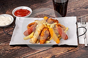 Snack plate with french fries, crispy chicken, cheese sticks, sausage and spring rolls on wooden table