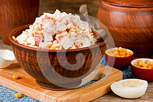 Snack salad from corn, egg, crab stick in a clay bowl on a wooden table