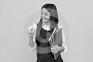 Snack time. Happy girl look at apple holding schoolbooks. School snack. Food education