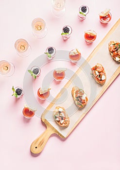 Snacks, brushetta sandwiches, gazpacho shots, desserts over pastel pink background