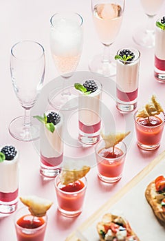 Snacks, brushetta sandwiches, gazpacho shots, desserts over pastel pink background