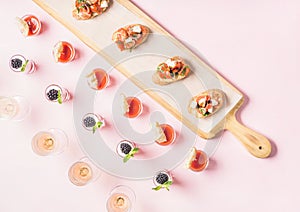 Snacks, brushetta sandwiches, gazpacho shots, desserts over pastel pink background