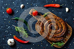 Snail sausage baked in an old oven is on a wooden board with pepper , garlic and rosemary