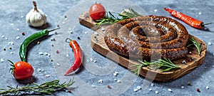 Snail sausage baked in an old oven is on a wooden board with pepper , garlic and rosemary