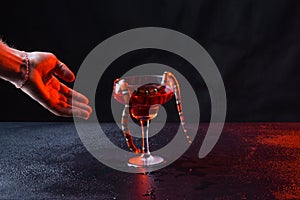 Snake in a glass with red liquid and a male brutal hand against a dark background