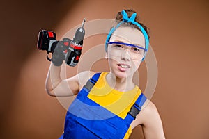 Snappy young Caucasian woman in work clothes with a scarf on her head and goggles with a screwdriver in her hand looks