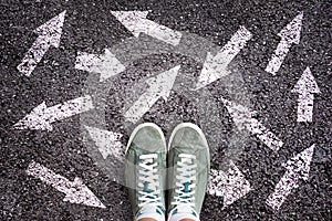 Sneaker shoes and arrows pointing in different directions on asphalt, choice concept photo